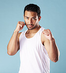 Handsome young hispanic man in a boxer pose standing in studio isolated against a blue background. Mixed race male athlete wearing a vest, ready for a fist fight or boxing match. A confident sportsman