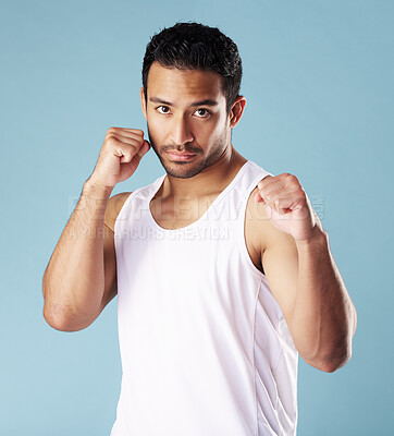 Handsome young hispanic man in a boxer pose standing in studio isolated against a blue background. Mixed race male athlete wearing a vest, ready for a fist fight or boxing match. A confident sportsman