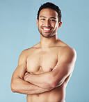 Handsome young hispanic man standing shirtless  in studio isolated against a blue background. Mixed race topless male athlete looking confident, healthy and fit. Exercising to increase his strength