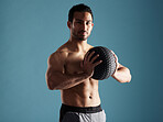 Handsome young hispanic man training with a medicine ball in studio isolated against a blue background. Mixed race shirtless male athlete exercising or working out to increase his strength and fitness