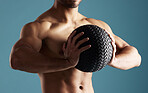 Closeup young hispanic man training with a medicine ball in studio isolated against a blue background. Mixed race shirtless male athlete exercising or working out to increase his strength and fitness