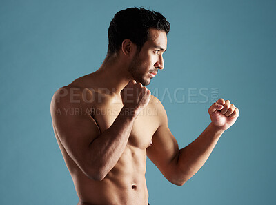 Buy stock photo Handsome young hispanic man standing shirtless in a boxer pose in studio isolated against a blue background. Mixed race topless male athlete, ready for boxing or a fist fight. A confident sportsman