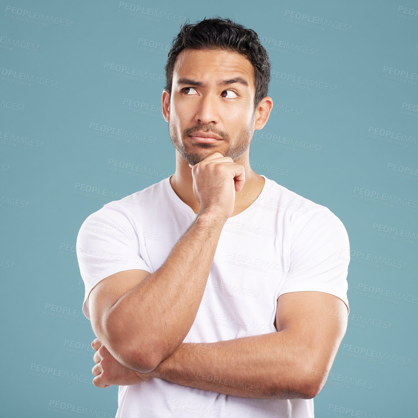 Buy stock photo Handsome young mixed race man looking thoughtful with his hand on his chin and looking away while standing in studio isolated against a blue background. Hispanic male thinking about a bright idea