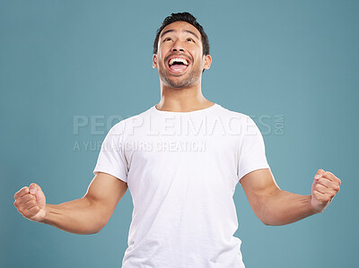Handsome young mixed race man celebrating victory or success while standing in studio isolated against a blue background. Hispanic male cheering and pumping his fists at success or achievement