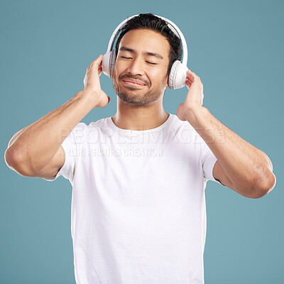 Buy stock photo Handsome young mixed race man listening to music while standing in studio isolated against a blue background. Hispanic male streaming his favourite playlist online using wireless headphones