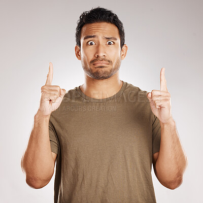 Handsome young mixed race man pointing towards copyspace while standing in studio isolated against a grey background. Unsure hispanic male advertising or endorsing your product, company or idea