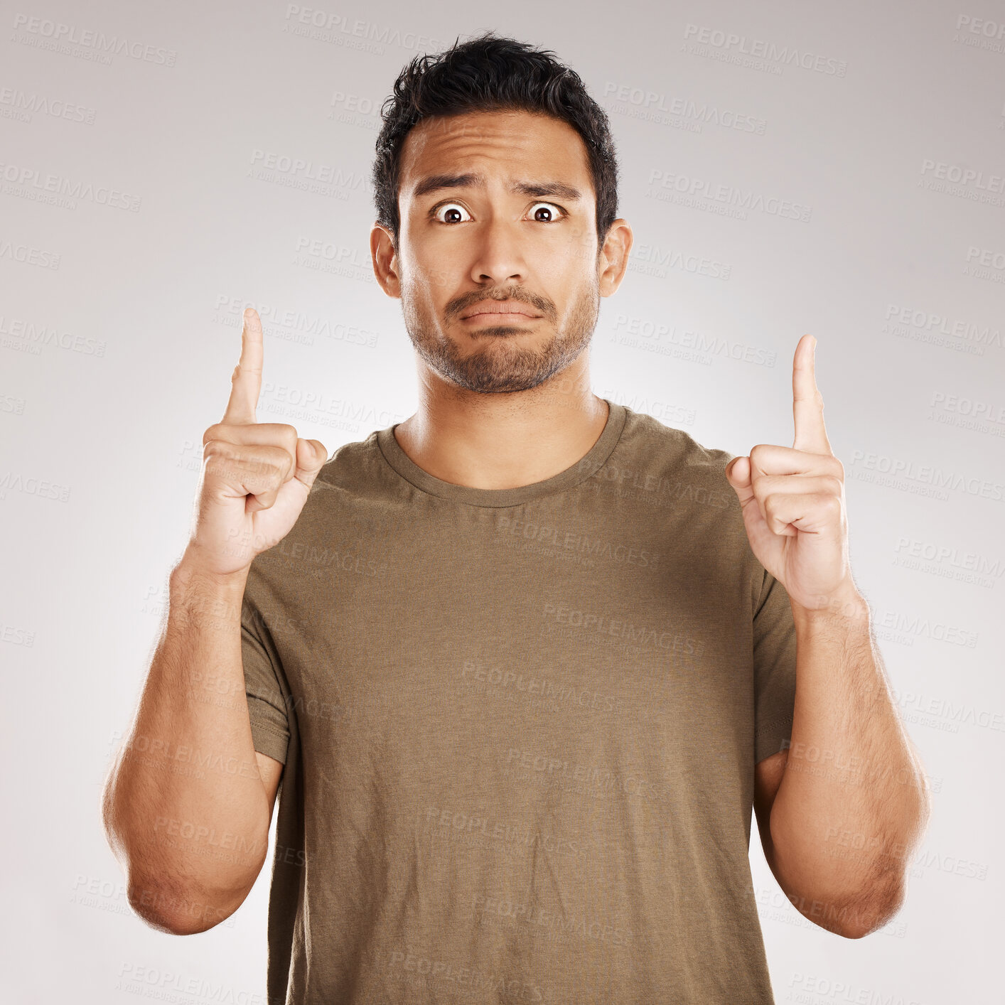Buy stock photo Handsome young mixed race man pointing towards copyspace while standing in studio isolated against a grey background. Unsure hispanic male advertising or endorsing your product, company or idea
