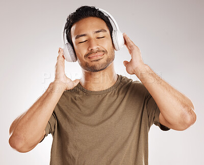 Buy stock photo Handsome young mixed race man listening to music while standing in studio isolated against a grey background. Hispanic male streaming his favourite playlist online using wireless headphones