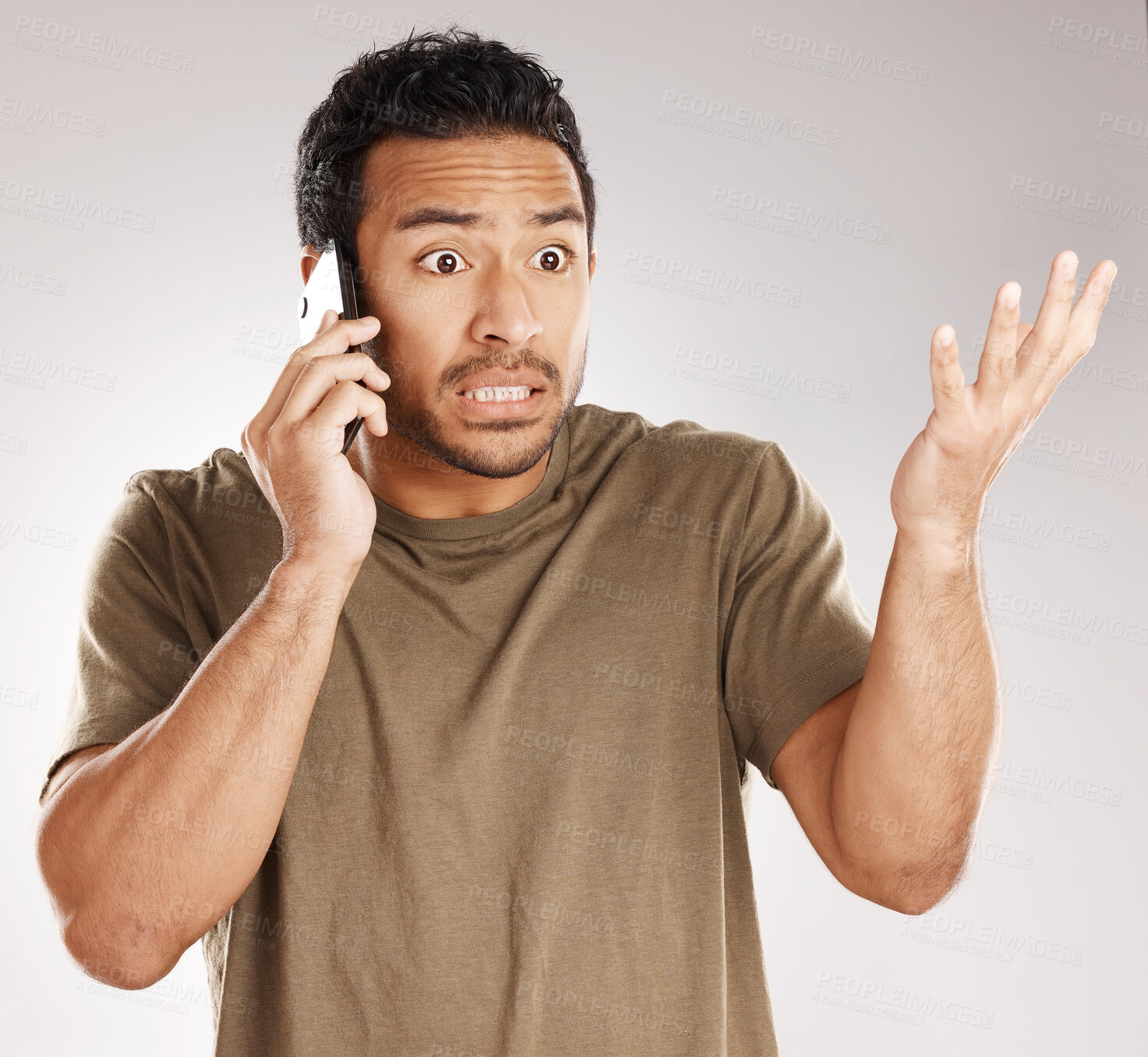 Buy stock photo Handsome young mixed race man looking irritated, aggravated or agitated while using his phone in studio isolated against a grey background. Displeased hispanic male making a call to complain or argue
