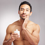 Handsome young mixed race man shirtless in studio isolated against a grey background. Hispanic male applying aftershave after shaving. Take care of your skin when you groom or shave your beard and face