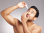 Closeup young mixed race man shirtless in studio isolated against a grey background. Hispanic male applying eyedrops to his eyes. Taking caring of his vision and sight as instructed by the optometrist