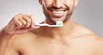 Closeup young mixed race man shirtless in studio isolated against a grey background. Hispanic male brushing his teeth. Taking caring of mouth and oral hygiene to promote dental health and healthy gums