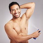 Handsome young mixed race man shirtless in studio isolated against a grey background. Hispanic male applying deodorant to his underarms. Healthy and fresh, making sure to look and smell clean