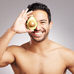 Handsome young mixed race man posing with an avocado isolated in studio against a grey background. His skincare regime keeps him fresh. For firm skin, eat healthy. Packed with vitamins and nutrients