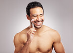 Handsome young mixed race man posing shirtless in studio isolated against a grey background. Hispanic male using a dermal face roller to massage and relax his skin. All part of his skincare regime