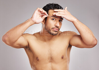 Buy stock photo Handsome young mixed race man posing shirtless in studio isolated against a grey background. Hispanic male plucking his eyebrows with a tweezers. All part of his daily grooming and skincare routine