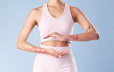 Buy stock photo Closeup mixed race fitness woman gesturing around her tummy in studio against a blue background. Young hispanic female athlete with hands placed around her stomach. A good diet promotes gut health