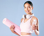 Mixed race fitness woman standing with her yoga mat and water bottle in studio against a blue background. Beautiful young hispanic female athlete exercising or working out. Health and fitness