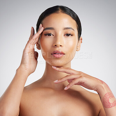 Portrait of a beautiful mixed race woman touching smooth soft skin in a studio. Hispanic model with healthy natural glowing skin looking confident against grey copyspace while doing routine skincare