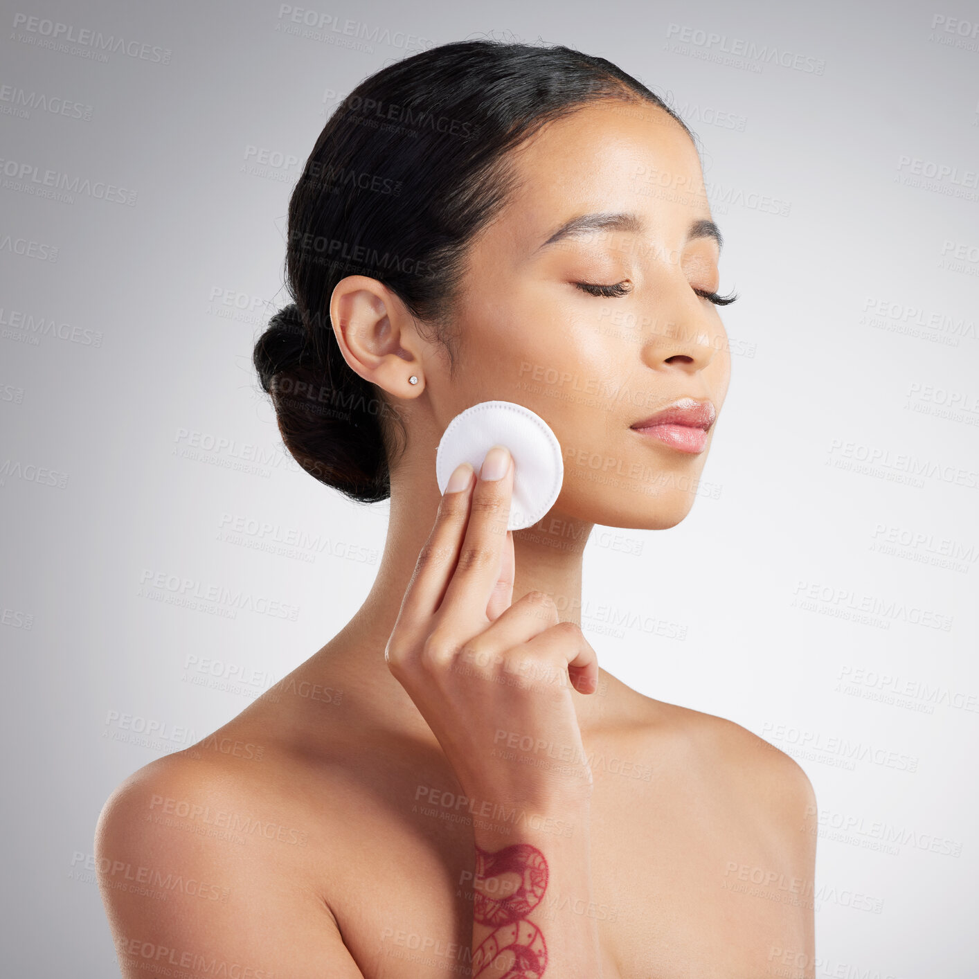 Buy stock photo A beautiful mixed race woman using a cotton pad to remove makeup during a selfcare grooming routine. Hispanic woman applying toner to her face against grey copyspace background in a studio