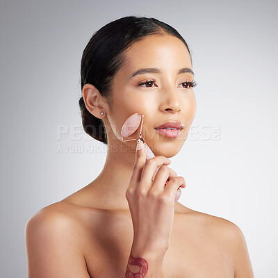 Buy stock photo A beautiful mixed race woman using a rose quartz derma roller during a selfcare grooming routine. Young hispanic woman using anti ageing tool against grey copyspace background