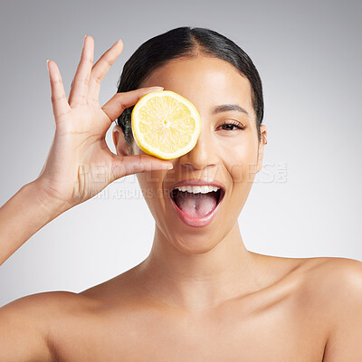 Studio Portrait of a happy smiling mixed race woman holding a lemon. Hispanic model promoting the skin benefits of a healthy diet against a grey copyspace background