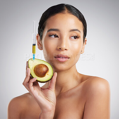 A gorgeous mixed race woman holding an avocado and syringe. Hispanic model promoting the skin benefits of avocado extract against a grey copyspace background