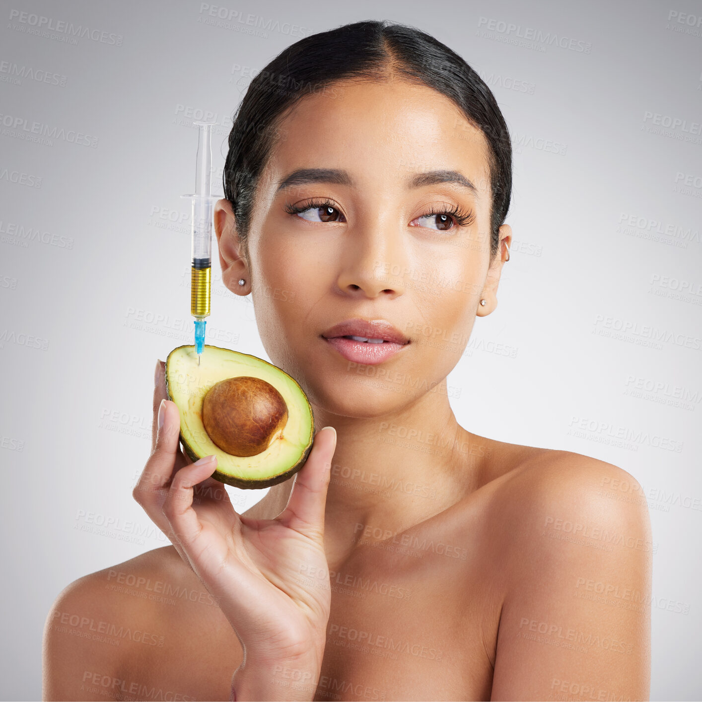 Buy stock photo A gorgeous mixed race woman holding an avocado and syringe. Hispanic model promoting the skin benefits of avocado extract against a grey copyspace background