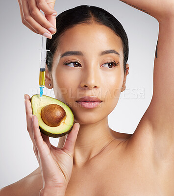 A gorgeous mixed race woman holding an avocado and syringe. Hispanic model promoting the skin benefits of avocado extract against a grey copyspace background