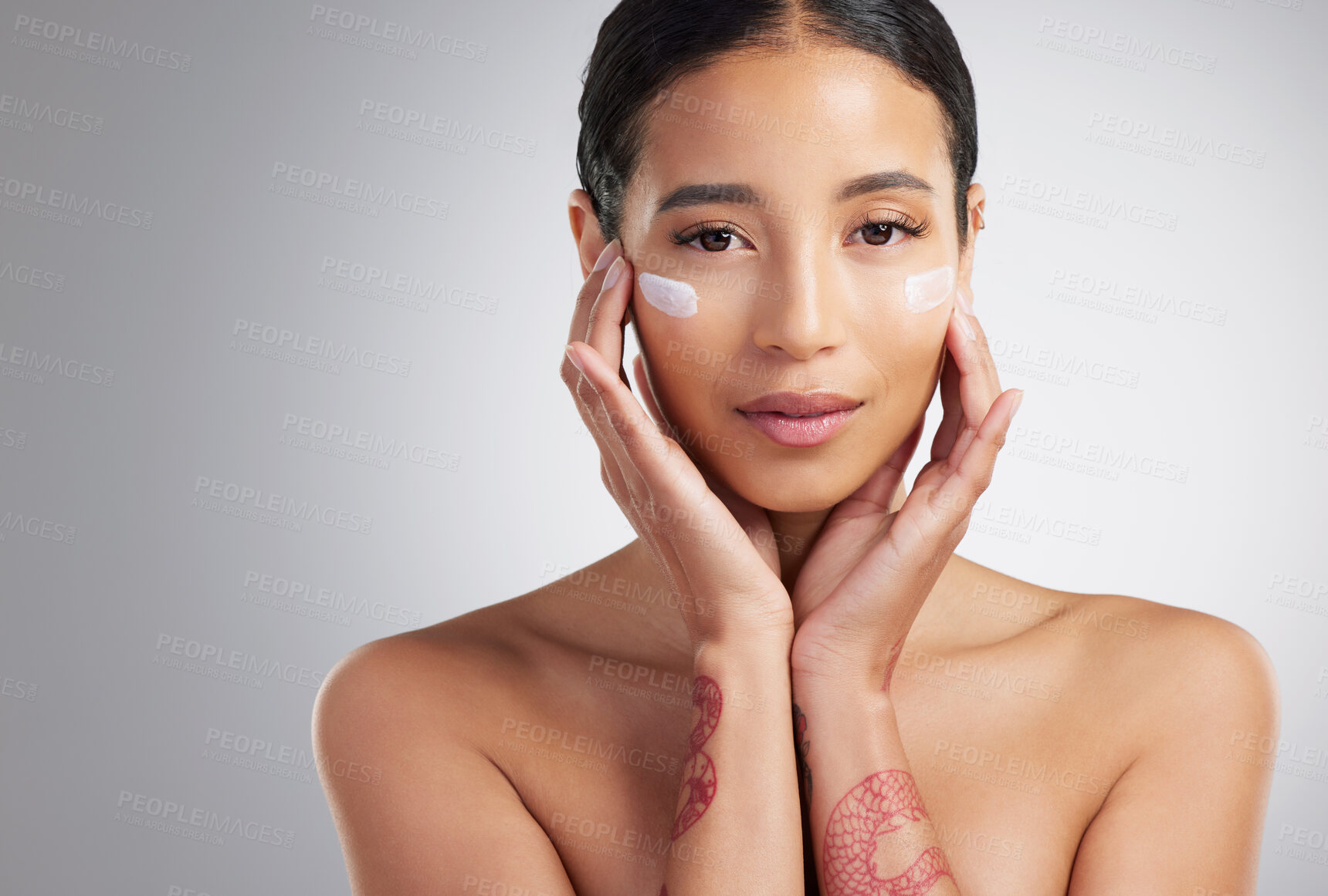 Buy stock photo Studio Portrait of a beautiful smiling mixed race woman applying cream to her face. Hispanic model with glowing skin using sunscreen against a grey copyspace background