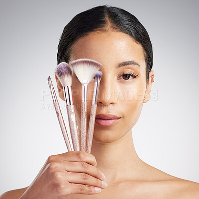 Studio Portrait of a beautiful mixed race woman posing with a collection of makeup brushes during pamper routine. Hispanic model with cosmetic tools standing against a grey copyspace background
