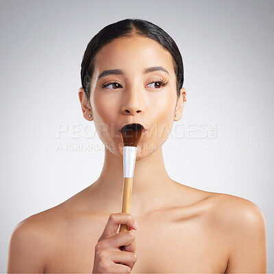 A beautiful mixed race woman posing with a makeup brush during a pamper routine. Hispanic model holding a contouring brush against a grey copyspace background