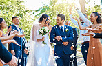 Wedding guests throwing rose petals confetti tradition over bride and groom on their special day. Newlywed couple walking past friends and family