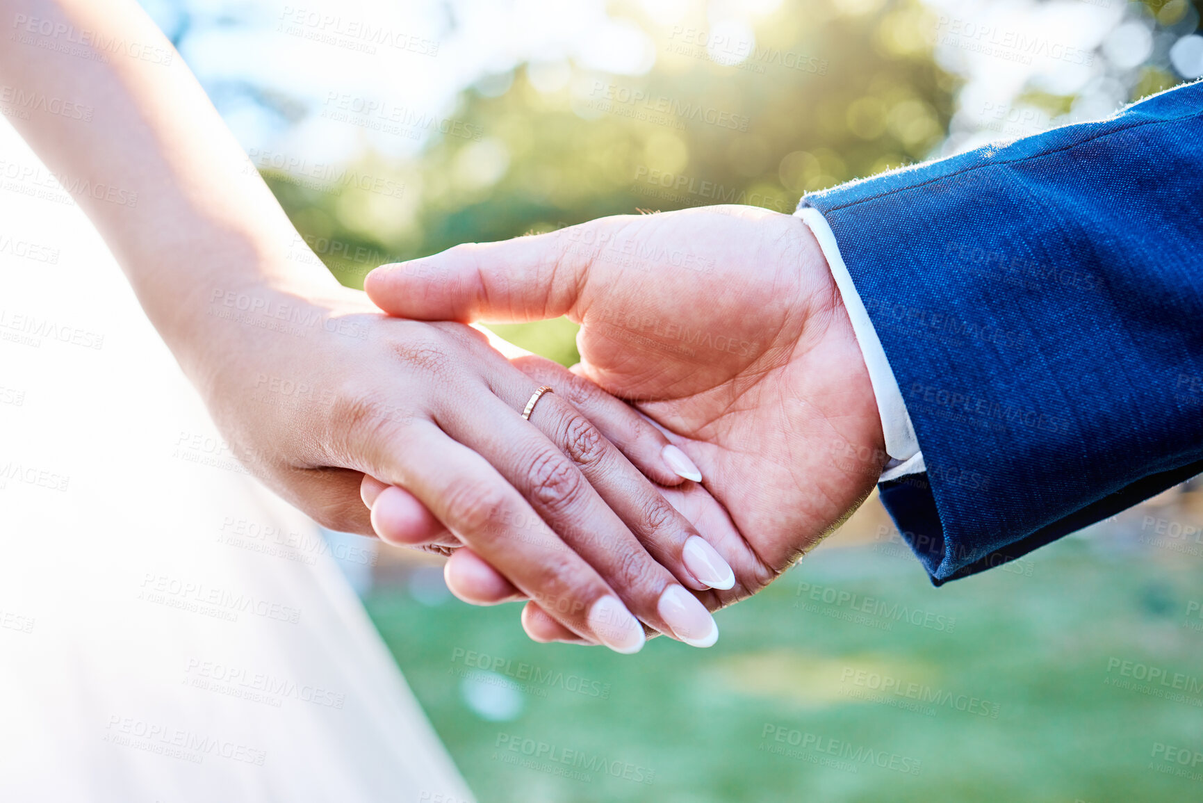 Buy stock photo Close up hands of newlywed couple standing outside on a sunny day. Groom holding his brides hand with wedding band