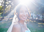 Stunning mixed race bride smiling while posing against greenery on a sunny day. A happy bride wearing a veil with beautiful brown locks in a up-style and natural make-up