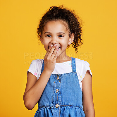 Studio portrait mixed race girl laughing with her hand over her mouth isolated against a yellow background. Cute hispanic child posing inside. Happy and carefree kid finding the funny side of things