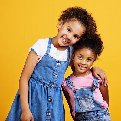 Studio portrait mixed race girl sisters isolated against a yellow background. Cute hispanic children posing inside. Happy and carefree kids standing together. Sisters, siblings and best friends