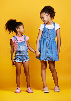 Mixed race girl sisters holding hands isolated against a yellow background. Cute hispanic children posing inside. Happy and carefree kids standing together. Sisters, siblings and best friends
