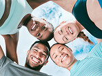 Portrait of a diverse group of happy sporty people from below joining their heads together in a huddle for support and unity with cloudy sky in the background. Cheerful motivated athletes ready for exercise workout outside