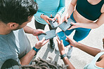 Closeup of diverse group of sporty people from above using cellphones with blank screens in synchronicity while standing in a circle around each other. Hands of athletes browsing online and searching the internet in a huddle. Downloading and sharing media