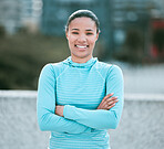 Portrait of one confident young mixed race woman standing with arms crossed ready for exercise outdoors. Determined female athlete looking happy and motivated for training workout in the city