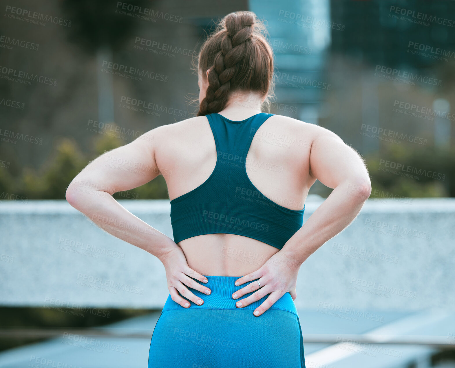 Buy stock photo One caucasian woman from behind holding sore lower back while exercising outdoors. Female athlete suffering with painful spine injury from fractured joint and inflamed muscles during workout. Struggling with stiff body cramps causing discomfort and strain