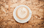 Closeup of a cup of hot coffee from above topped with frothy steamed milk in a creative pattern on a wooden table in a cafe. Warm drink in teacup on saucer with latte and cappuccino art