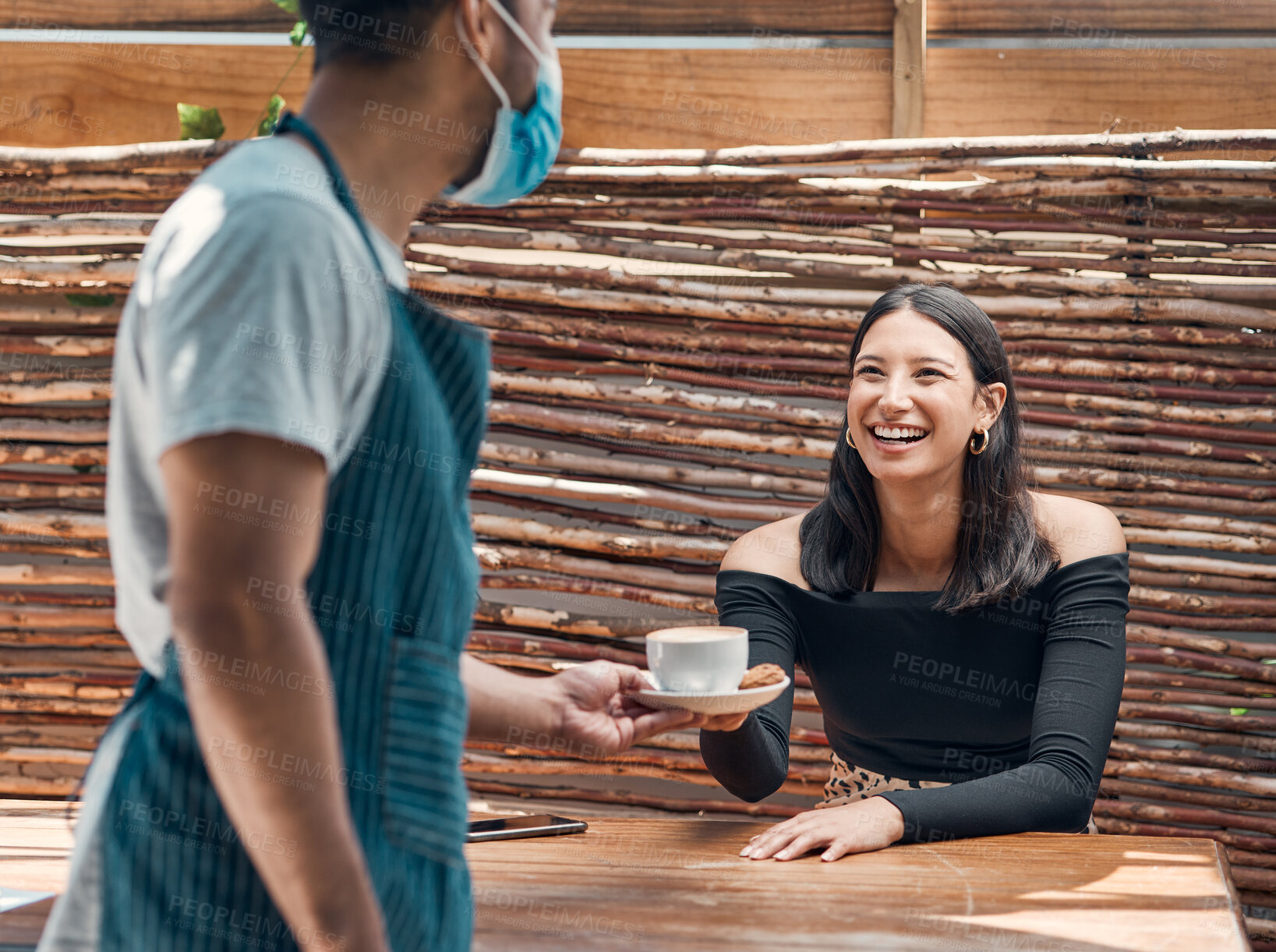 Buy stock photo Happy young hispanic woman receiving a cup of coffee from a waiter wearing a face mask in a local cafe. Mixed race woman excited to be served her warm latte or cappuccino order while relaxing at a restaurant during the covid pandemic