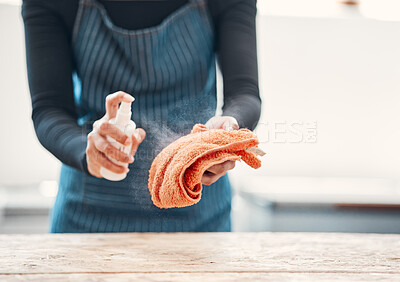 Closeup of one woman spraying antibacterial cleaner from a bottle onto a cloth to disinfect and wipe table in a cafe or store. Hands of a shop assistant sanitising surfaces to maintain hygiene and prevent the spread of covid germs