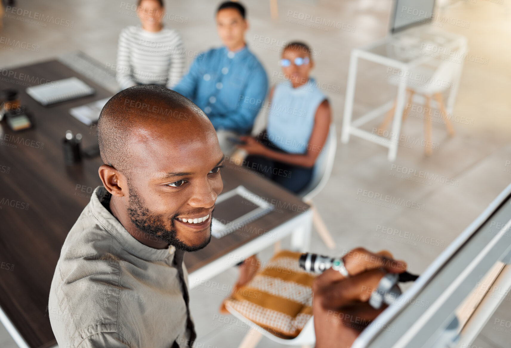 Buy stock photo Group of diverse businesspeople having a meeting in an office at work. Young happy african american businessman smiling while writing an idea on a whiteboard in a boardroom with colleagues. Businesspeople planning together