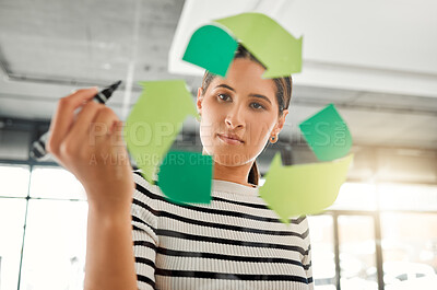 Young focused mixed race businesswoman drawing a recycle symbol on a glass window in an office at work. One serious hispanic businessperson drawing a sign for awareness to recycling