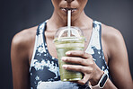 Closeup of one active woman drinking a healthy green detox smoothie while exercising outdoors. Female athlete sipping on fresh fruit juice with straw in plastic cup to cleanse and provide energy for training. Wholesome drink with vitamins and nutrients
