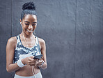 One happy young mixed race woman listening to music with earphones from cellphone while on a break from exercise with copyspace against a dark background. Confident female athlete texting and using fitness apps online while browsing social media outdoors