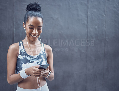 Buy stock photo One happy young mixed race woman listening to music with earphones from cellphone while on a break from exercise with copyspace against a dark background. Confident female athlete texting and using fitness apps online while browsing social media outdoors